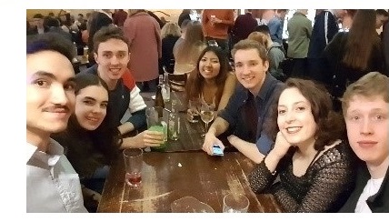 A group of students sat around a table, smiling at the camera.