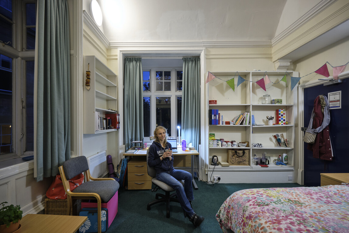 Student on swivel chair by desk, holding cup of tea