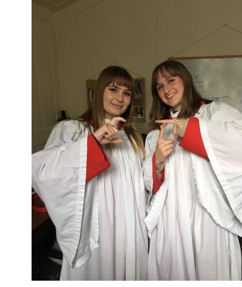Two female members of the Choir of Christ's College, Cambridge in choir robes.