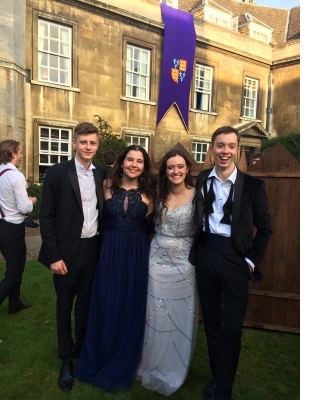 Two men in black tie (left and right) and two women in ballgowns (centre) with their arms around each other, during a May Ball, in First Court of Christ's College, Cambridge.