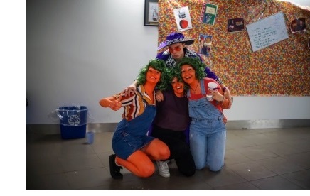 Three women dressed as Oompa Loompas and a man dressed as Mike TV, posing for a photo with their arms around each other.