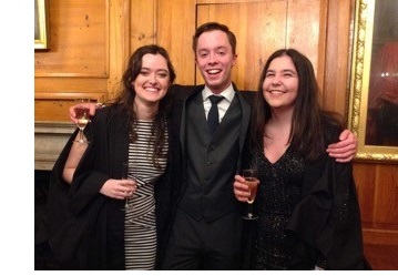 Two female student (left and right) and a male student (centre) posing together in formal wear and academic gowns.