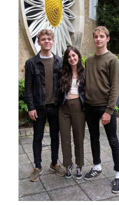 Two men (left and right) and one woman (centre), with their arms around each other, outside.