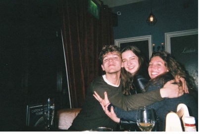 Three students hugging each other, sat in a bar.