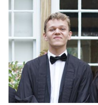 A headshot of a man, in a tuxedo and academic gown, smiling.