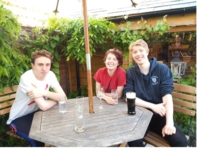 Two young men and a young women sat at a table in a pub garden with pints.