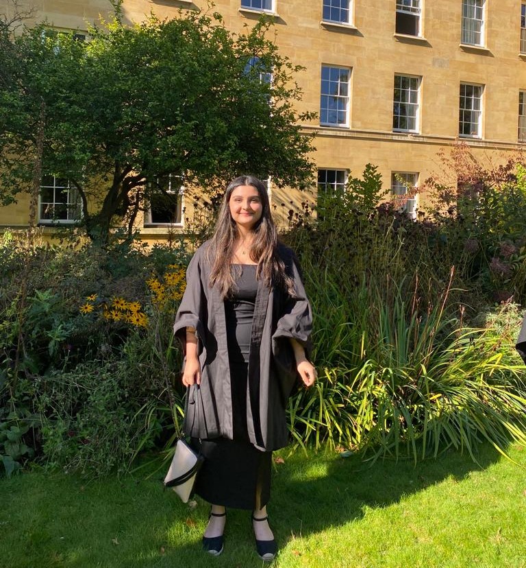 A student in a gown in front of some plants