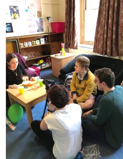 Olivia filming a girl sat in front of a birthday cake as other actors look on.