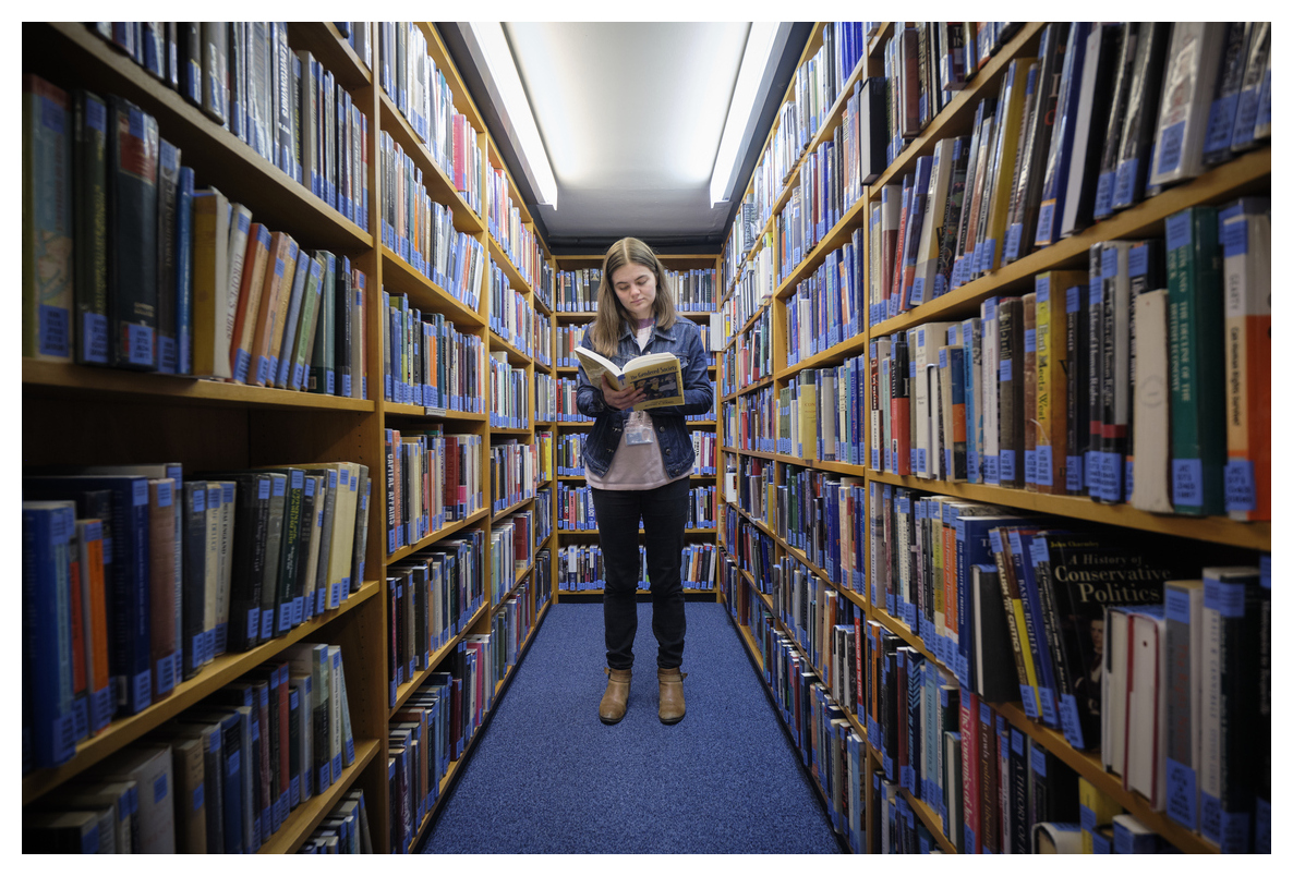 Student standing and reading between bookshelves