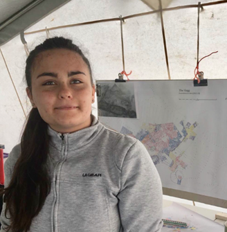 A student stands in a tent, with a map hanging behind her