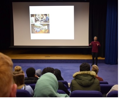 A man giving a presentation to prospective students in the Yusuf Hamied Lecture Theatre at Christ's College, Cambridge.