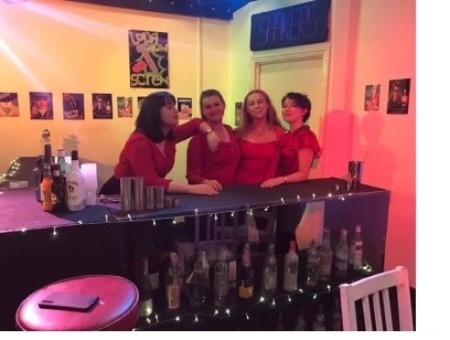 Olivia and three other actors in an ADC production of 'Shakers', posing behind a bar and lit by pink light.