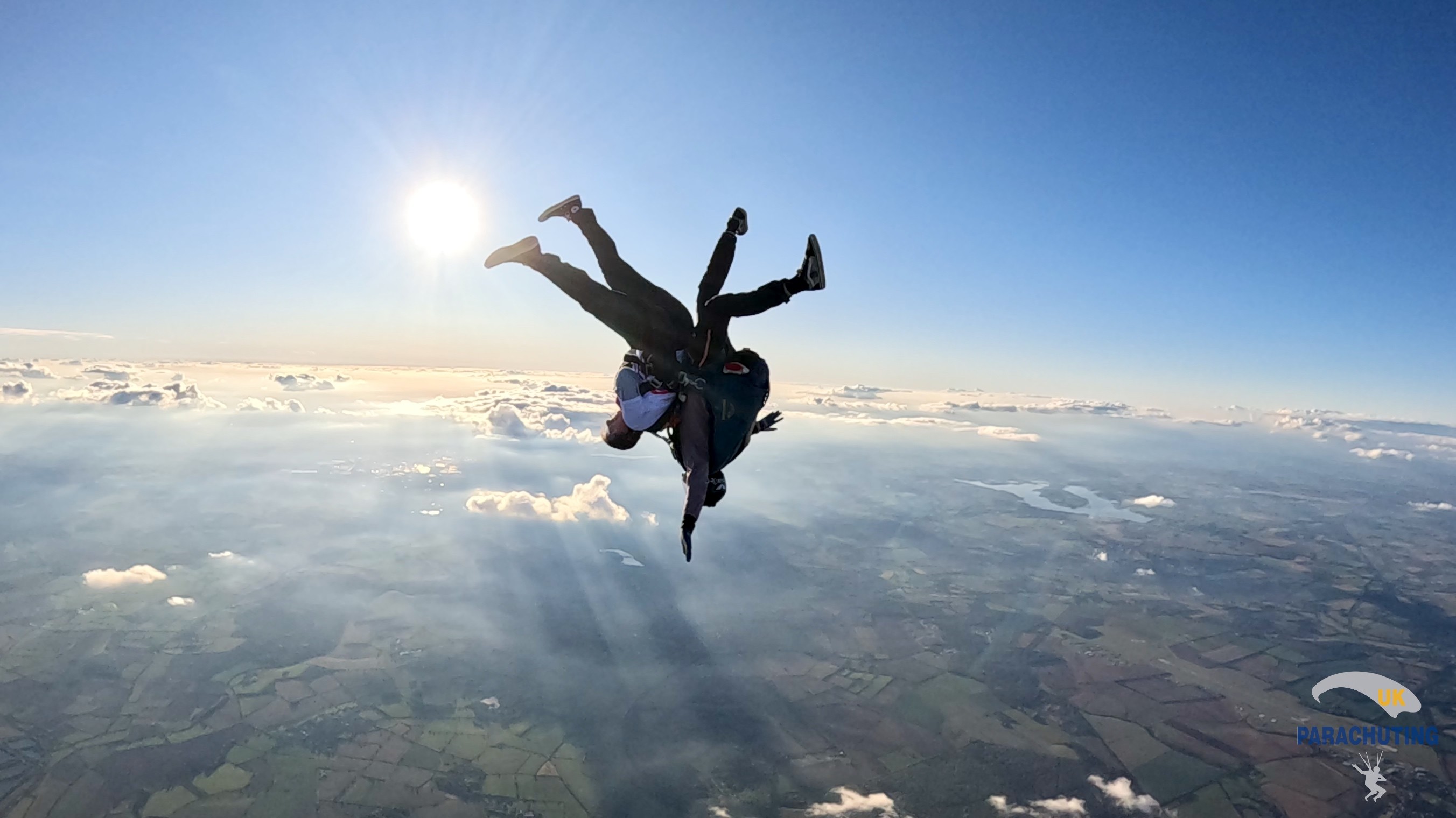 Two people skydiving upside down against a blue sky
