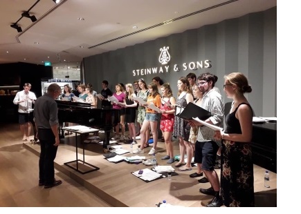 The choir of Christ's College Cambridge, dressed in casual clothes, onstage during a rehearsal for a concert.