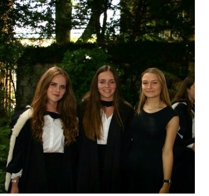 Anna and two other students in academic dress at graduation.