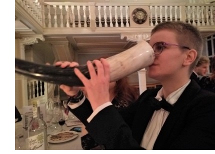A short-haired woman in black tie drinking from a mead horn