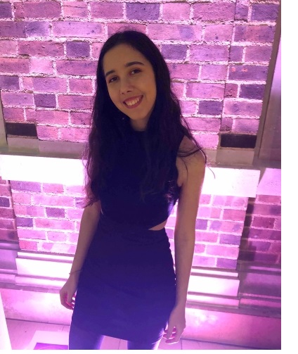 A photo of Yasmin, against a background of purple-lit bricks