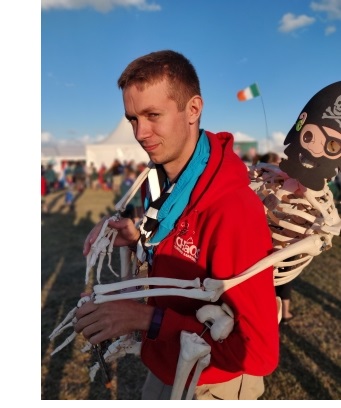A man in a red jacket giving a toy skeleton dressed as a pirate a piggyback.