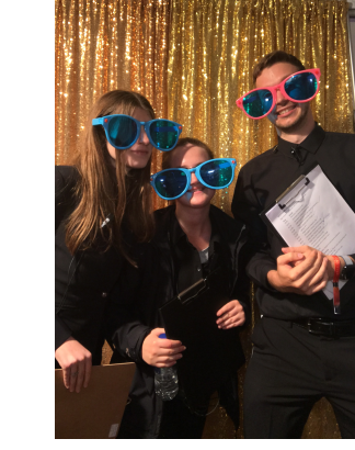 Three people, dressed in all black, wearing comically oversized sunglasses of varying colours in a photo booth.