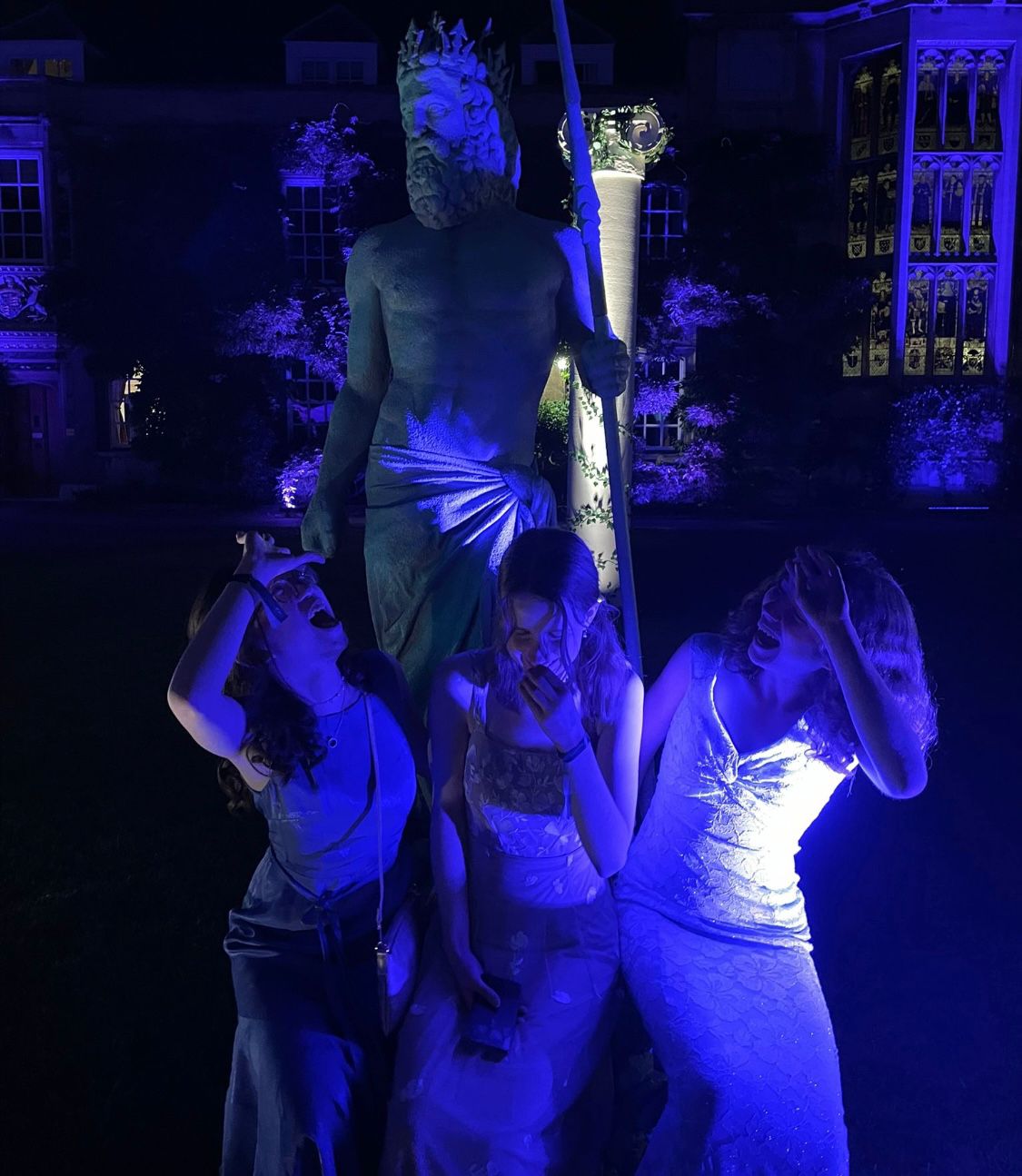 Blue lighting, three friends pose underneath a greek-style statue
