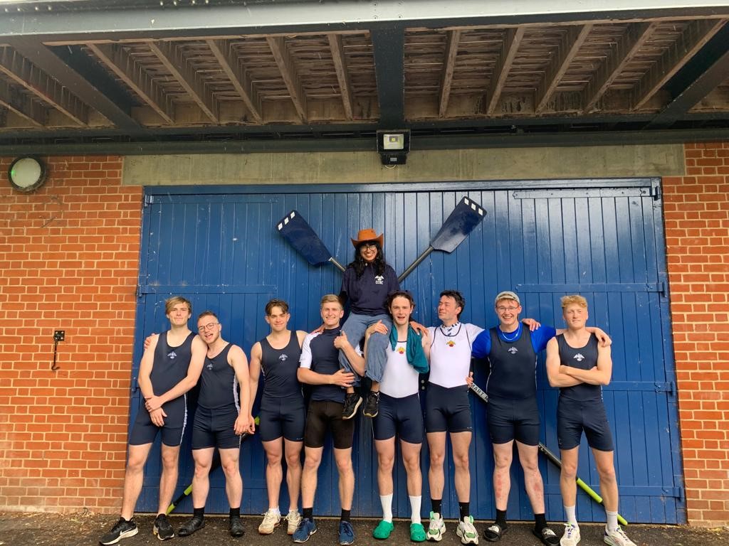 Eight men, with a woman sat on the shoulders of two in the middle, wearing rowing gear