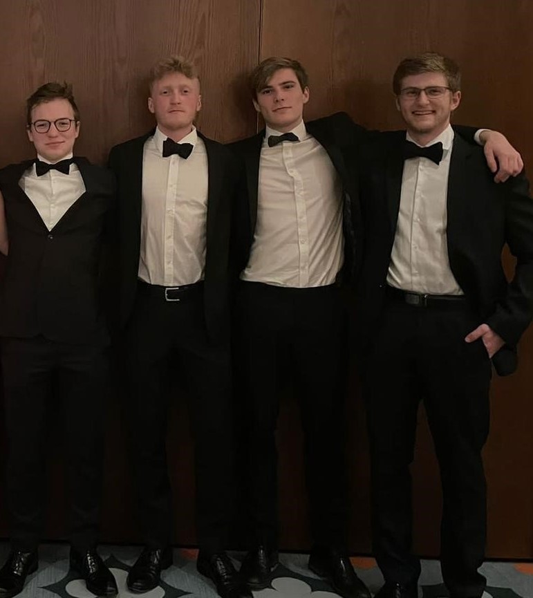 Four men in black tie pose in line for a photo