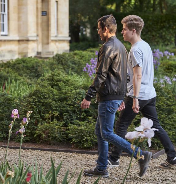Pair of male students chatting and walking through the garden in third court 