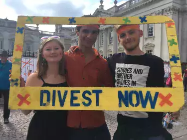 Esme and two friends posing with a sign that reads "DIVEST NOW".
